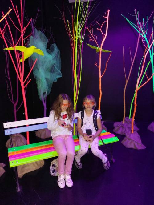 Na zdjęciu: dzieci wśród kolorowych świateł, siedzące na ławce